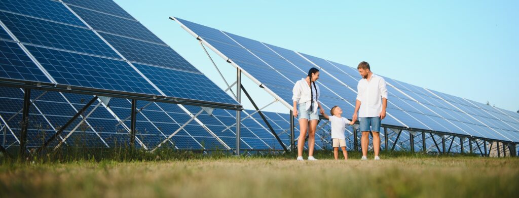 A wide shot of a happy family standing together and smiling at camera with a large solar panel